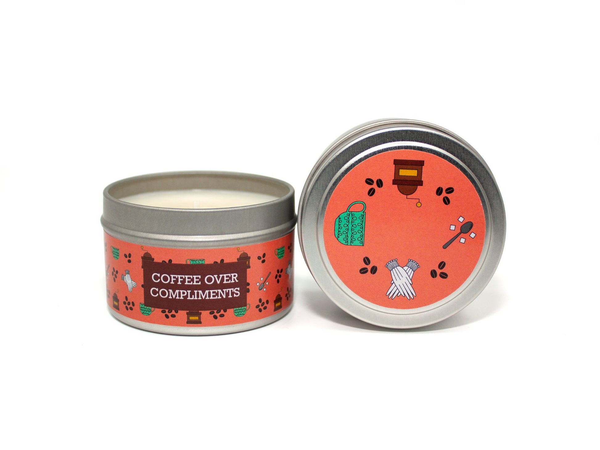 Onset & Rime cappucino scented candle called "Coffee Over Compliments" in a 4 oz silver tin. The circular label on top is coral with a pattern of coffee beans, a coffee grinder, white gloves and a spoon with sugar cubes. The text on the front label is "Coffee Over Compliments - Espresso, Steamed Milk, Cinnamon".