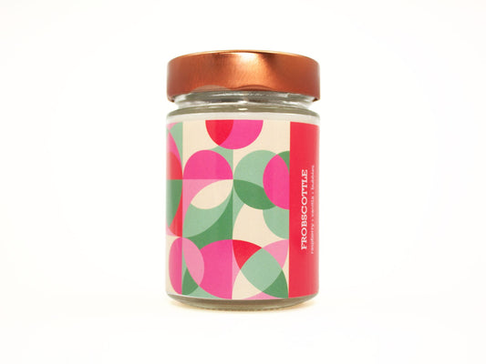 Onset & Rime fruity soda scented candle called "Frobscottle" in a 10 oz glass jar with copper lid. The label is a geometric pattern of overlapping pink, white and green circles and squares. The text on the label is "Frobscottle - Raspberry, Vanilla, Bubbles".