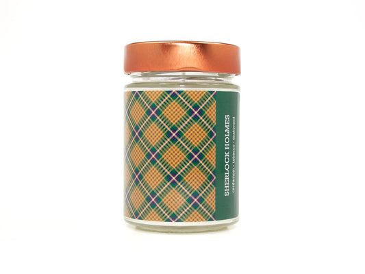 Onset & Rime woody tobacco scented candle called "Sherlock Holmes" in a 10 oz glass jar with copper lid. The label is a gold and green plaid pattern. The text on the label is "Sherlock Holmes - Cardamom, Tobacco, Teakwood".