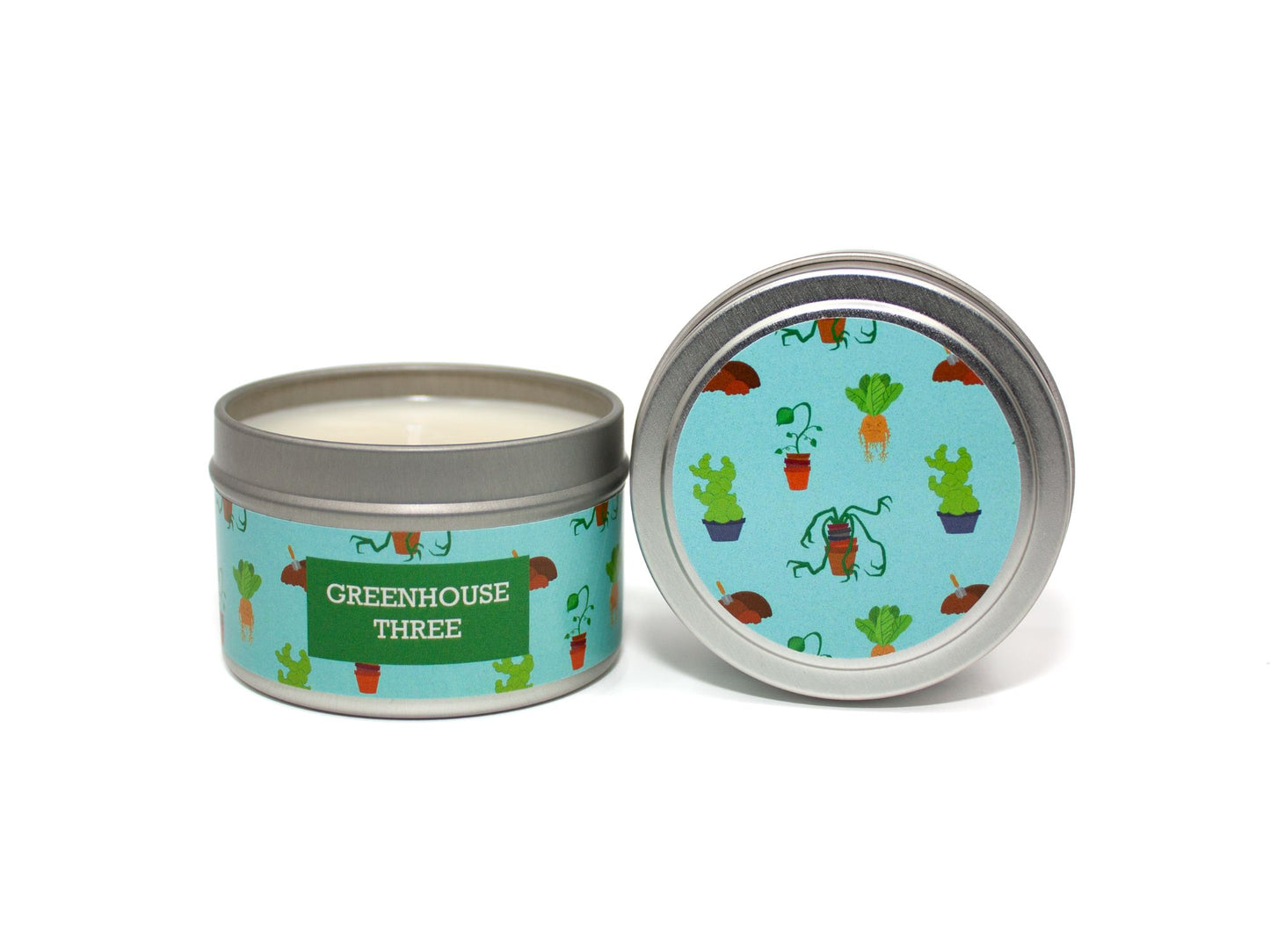 Onset & Rime foliage and earth scented candle called "Greenhouse Three" in a 4 oz silver tin. The circular label on top is sky blue featuring various magical plants. The text on the front label is "Greenhouse Three - Lush Foliage, Humid Air, Damp Earth".