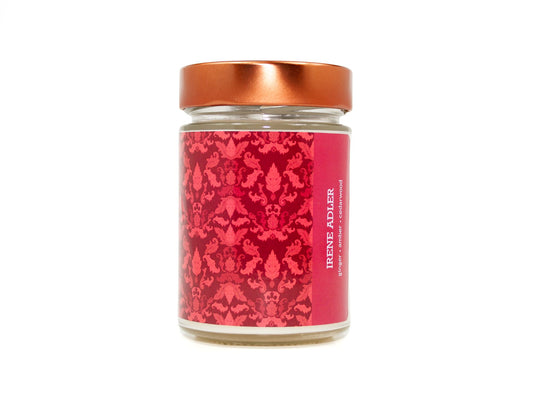 Onset & Rime ginger and amber scented candle called "Irene Adler" in a 10 oz glass jar with copper lid. The label is a deep red Victorian pattern. The text on the label is "Irene Adler - Ginger, Amber, Cedarwood".