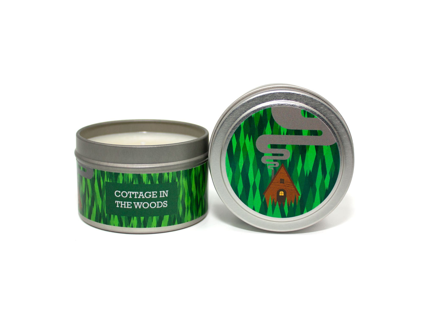 Onset & Rime pine and berries scented candle called "Cottage in the Woods" in a 4 oz silver tin. The circular label on top depicts a green pine forest and a small cottage with smoke rising from the chimney. The text on the front label is "Cottage in the Woods - Fir Trees, Forest Floor, Wild Berries".