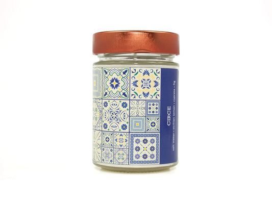 Onset & Rime lemon, cypress scented candle called "Circe" in a 10 oz glass jar with copper lid. The label is white with a dark blue Greek tile pattern. The text on the label is "Circe - Salt Water, Sicilian Lemon, Cypress, Fig".