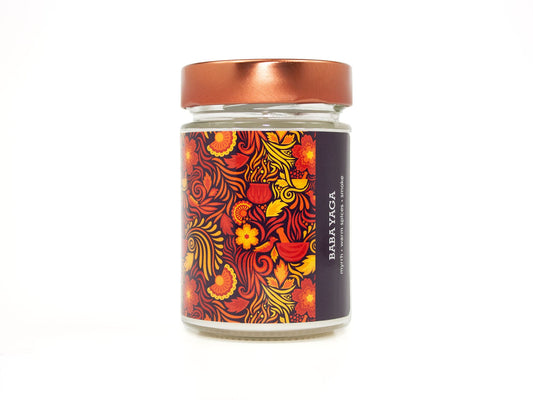 Onset & Rime spiced smoke scented candle called "Baba Yaga" in a 10 oz glass jar with copper lid. The label is purple-black with a bright red pattern of flames, swirls and flowers. The text on the label is "Baba Yaga - Myrrh, Warm Spices, Smoke".