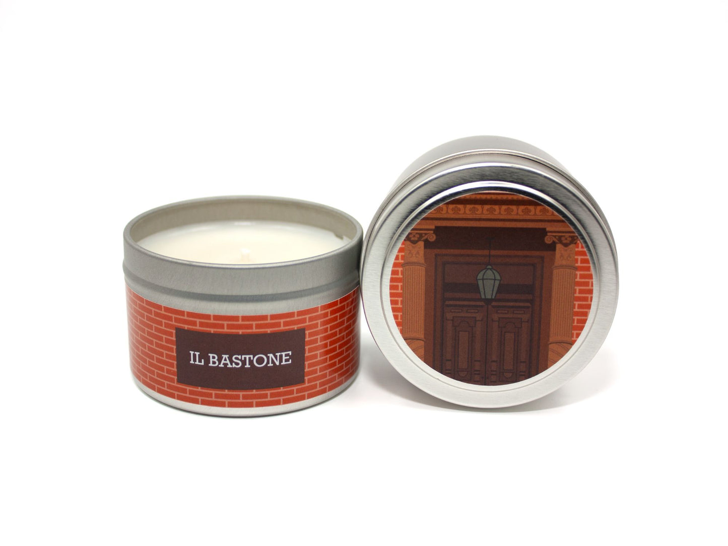 Onset & Rime apothocary scented candle called "Il Bastone" in a 4 oz silver tin. The circular label on top shows a detailed wood front door on a red brick house. The text on the front label is "Il Bastone - Orange Blossom, Verbena, Palo Santo, Cedar".