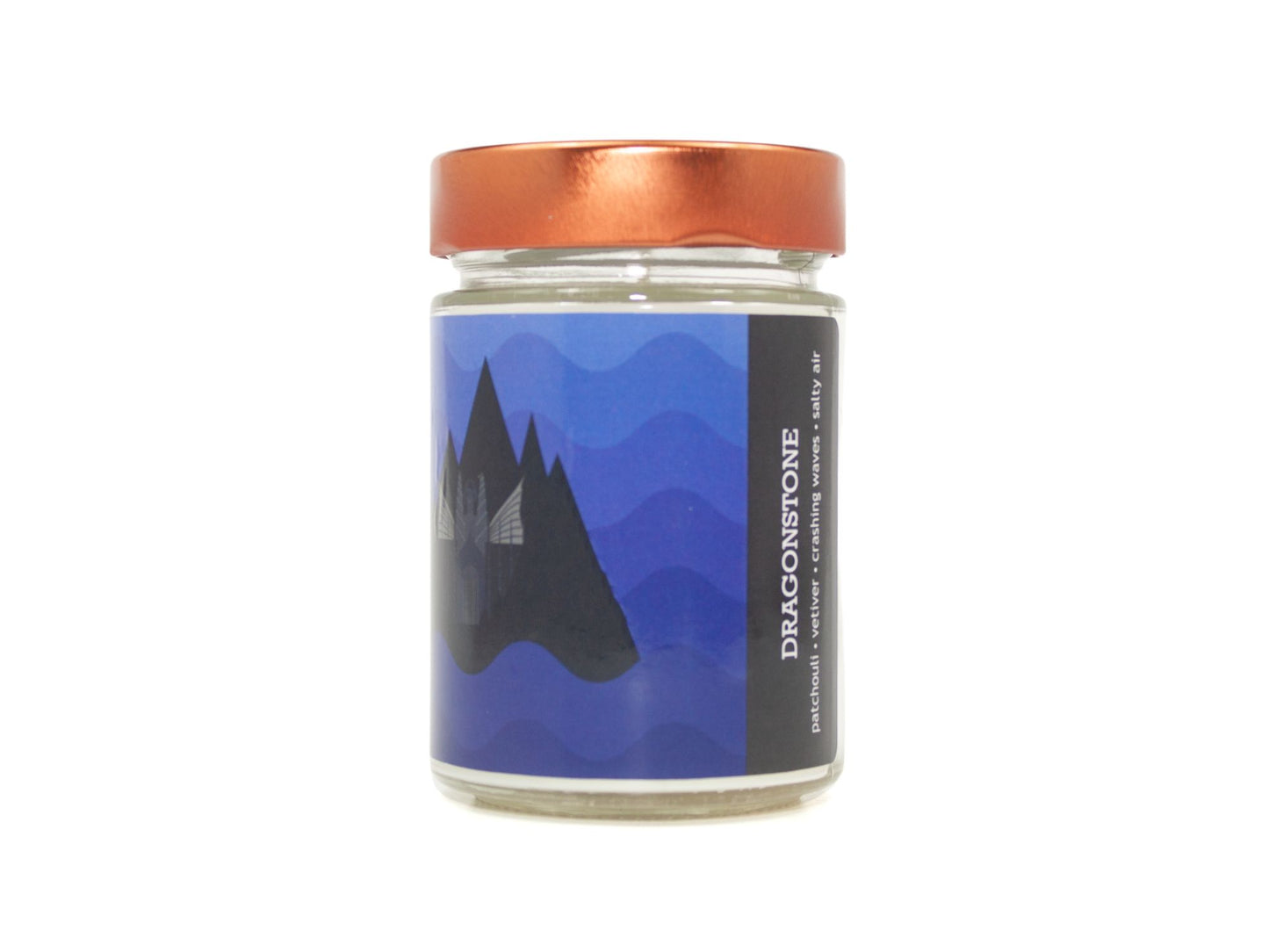 Onset & Rime chilly island scented candle called "Dragonstone" in a 10 oz glass jar with copper lid. The label has blue waves in the background with a volcanic island and castle. The text on the label is "Dragonstone - Patchouli, Vetiver, Crashing Waves, Salty Air".