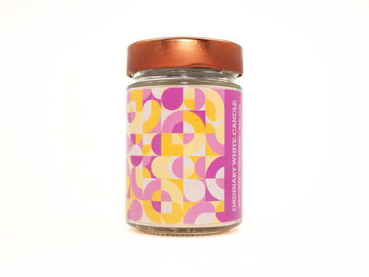 Onset & Rime flannel scented candle called "Ordinary White Candle" in a 10 oz glass jar with copper lid. The label is a geometric pattern of pink, yellow and white circles and teardrops. The text on the label is "Ordinary White Candle - Warm Flannel, Lemon Blossom, Sheer Musk".