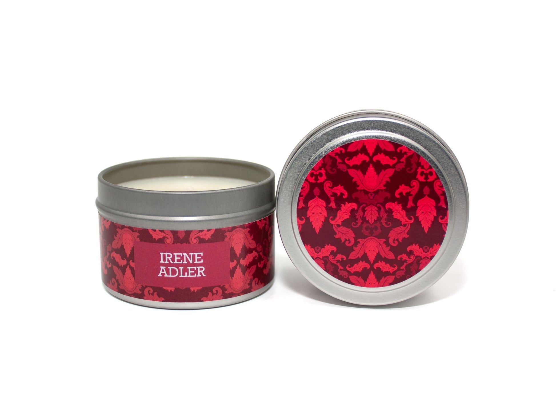 Onset & Rime ginger and amber scented candle called "Irene Adler" in a 4 oz silver tin. The circular label on top is a deep red Victorian pattern. The text on the front label is "Irene Adler - Ginger, Amber, Cedarwood".