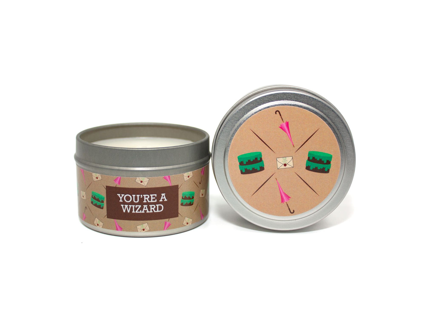 Onset & Rime chocolate cake scented candle called "You're a Wizard" in a 4 oz silver tin. The circular label on top is light brown with a pattern of pink umbrellas, white envelopes, and chocolate cakes with green icing. The text on the front label is "You're a Wizard - Chocolate Fudge Cake, Buttercream Frosting".