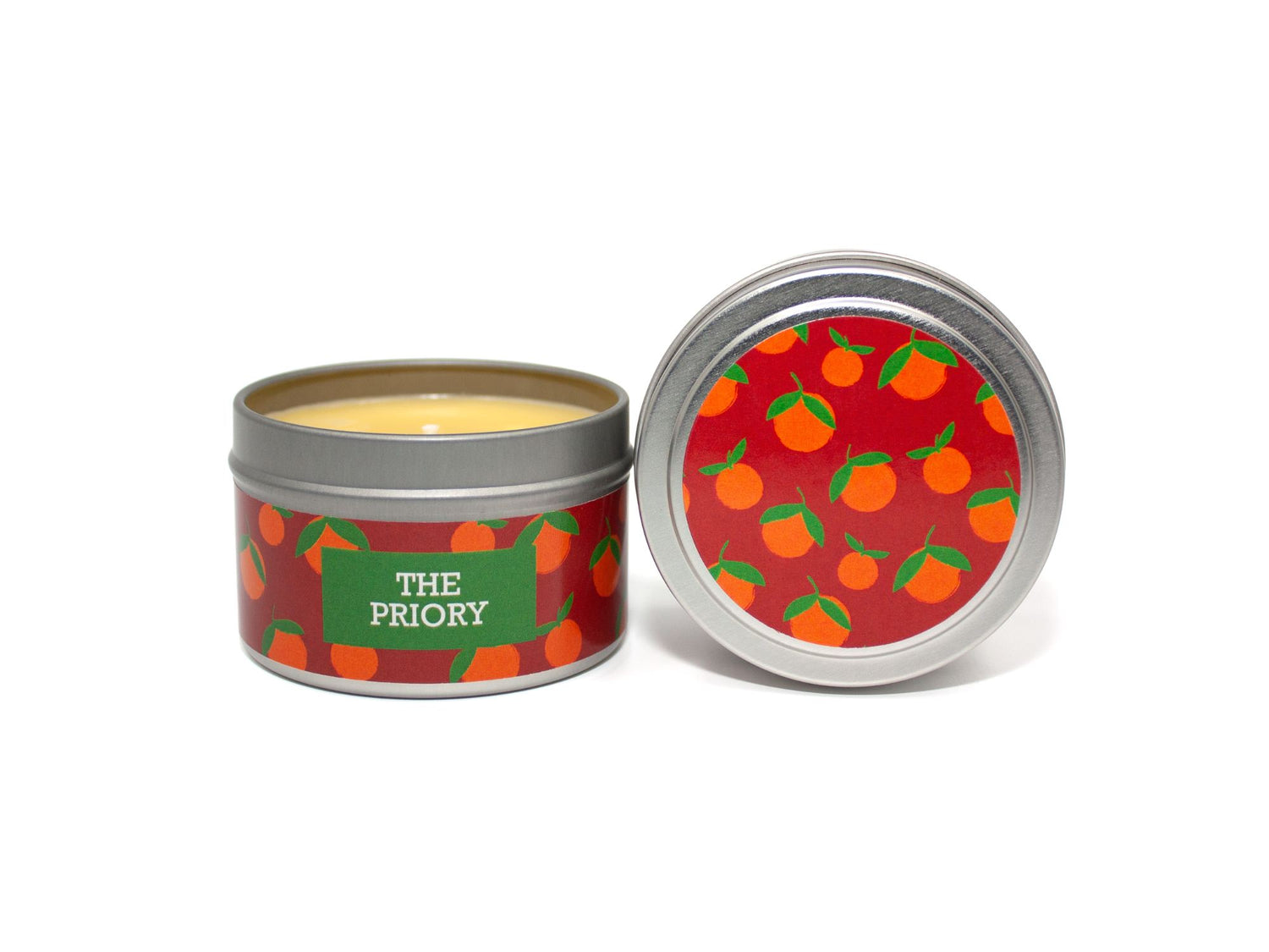 Onset & Rime spiced orange scented candle called "The Priory" in a 4 oz silver tin. The circular label on top is red with a pattern of oranges. The text on the front label is "The Priory - Orange, Cinnamon, Clove".