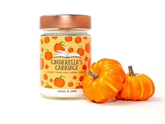 A staged photo of Onset & Rime pumpkin pie scented candle called "Cinderella's Carriage". The candle stands next to two mini pumpkins in front of a white background.