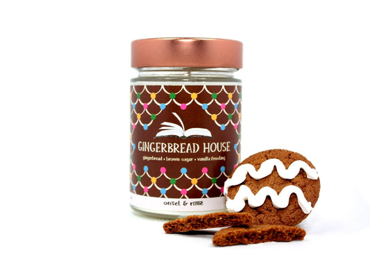 A staged photo of Onset & Rime gingerbread scented candle called "Gingerbread House". The candle stands next to decorated gingerbread cookies in front of a white background.